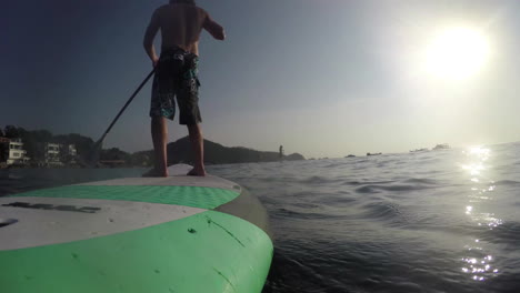 sup board riding. the camera is mounted on the back of the board. in the foreground a man rowing an oar