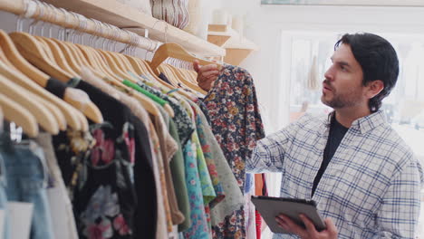 Propietario-Masculino-De-Una-Tienda-De-Moda-Usando-Una-Tableta-Digital-Para-Verificar-El-Stock-Sobre-Rieles-En-Una-Tienda-De-Ropa