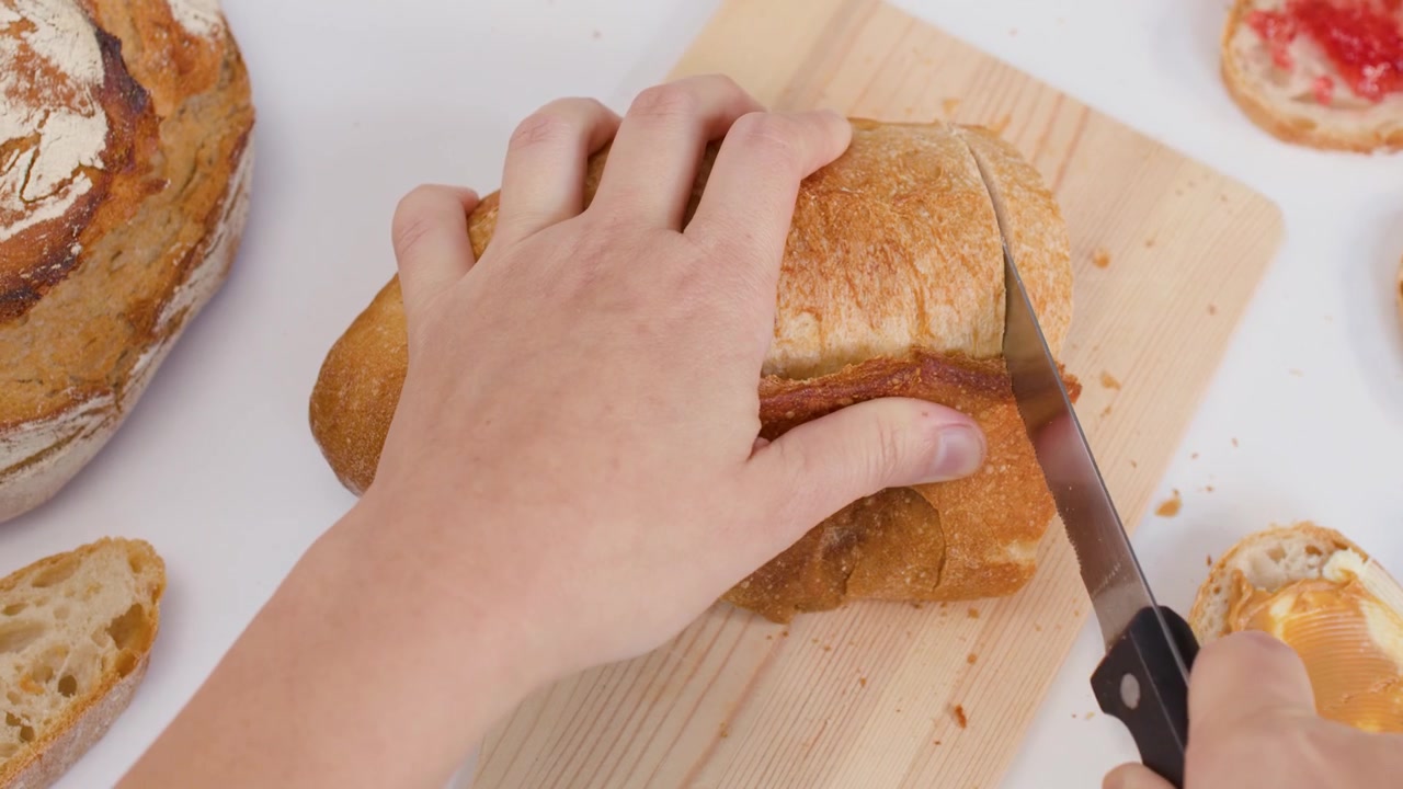 Person Slicing Fresh Loaf of Bread on Wooden Cutting Board