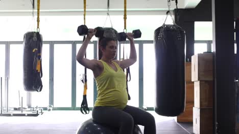 pregnant female model working out with weights in a gym to keep fit in her fourth trimester