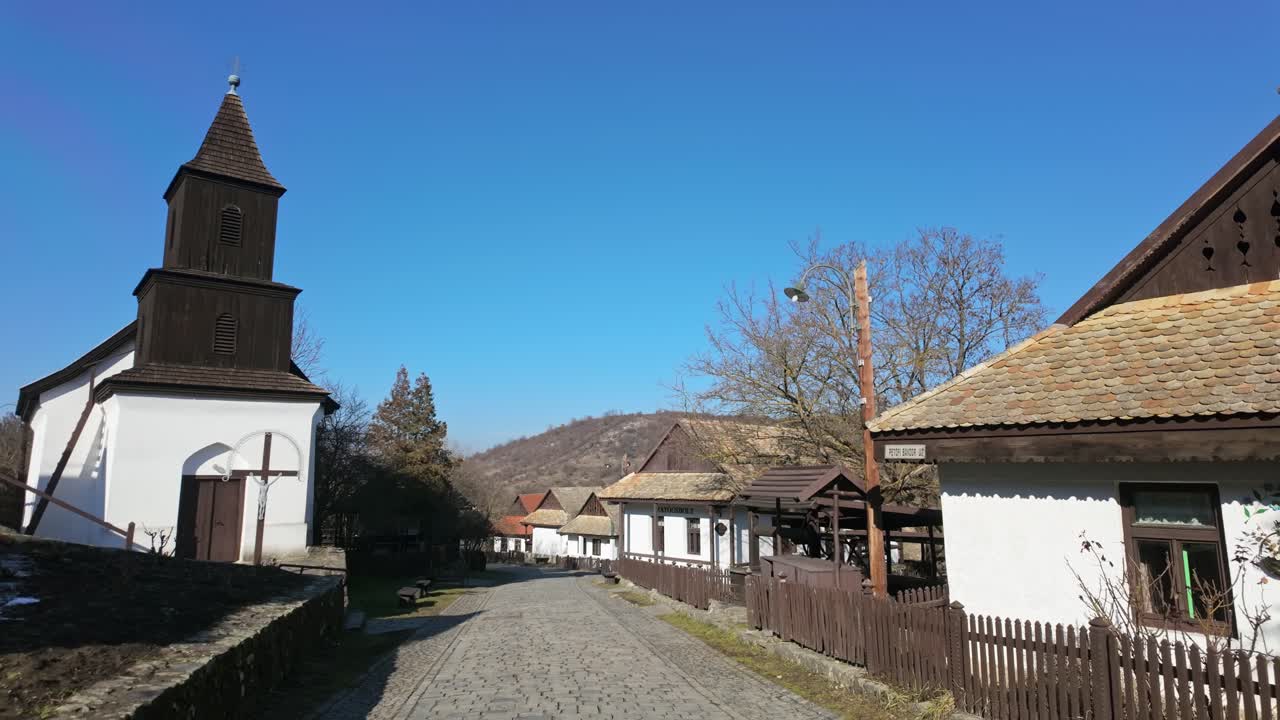 Street view from the Old Town of Holloko with a church and traditional paloc style of houses on a sunny day in Hungary.