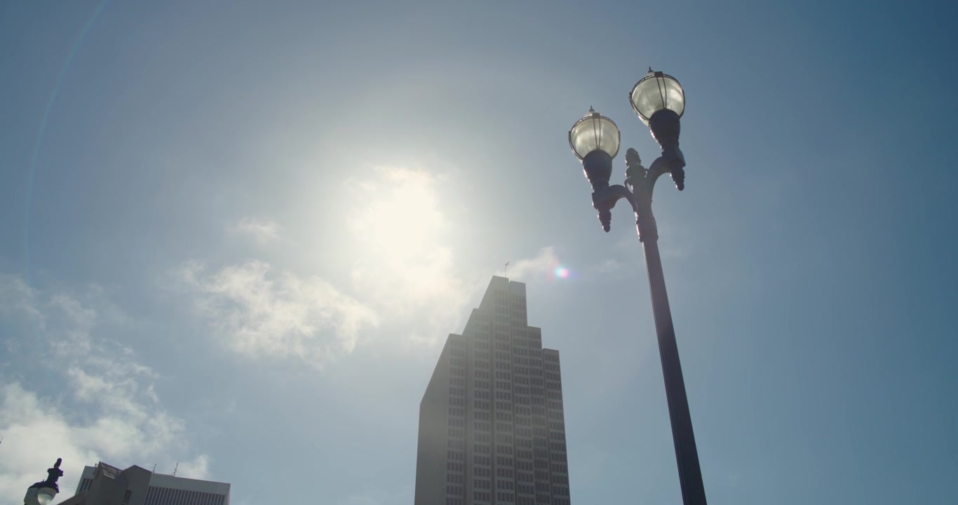Tampilan sinematik genggam 4K dari jalan setapak Embarcadero San Francisco, melihat ke arah bangunan perkotaan dan tiang lampu di sepanjang tepi laut dengan suar matahari yang menyilaukan.