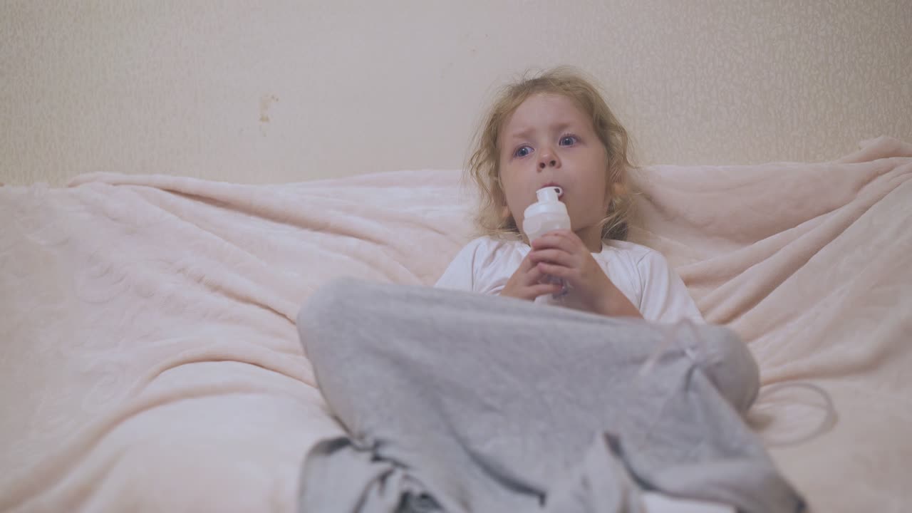 una bambina con un inalatore giace in un letto confortevole in camera