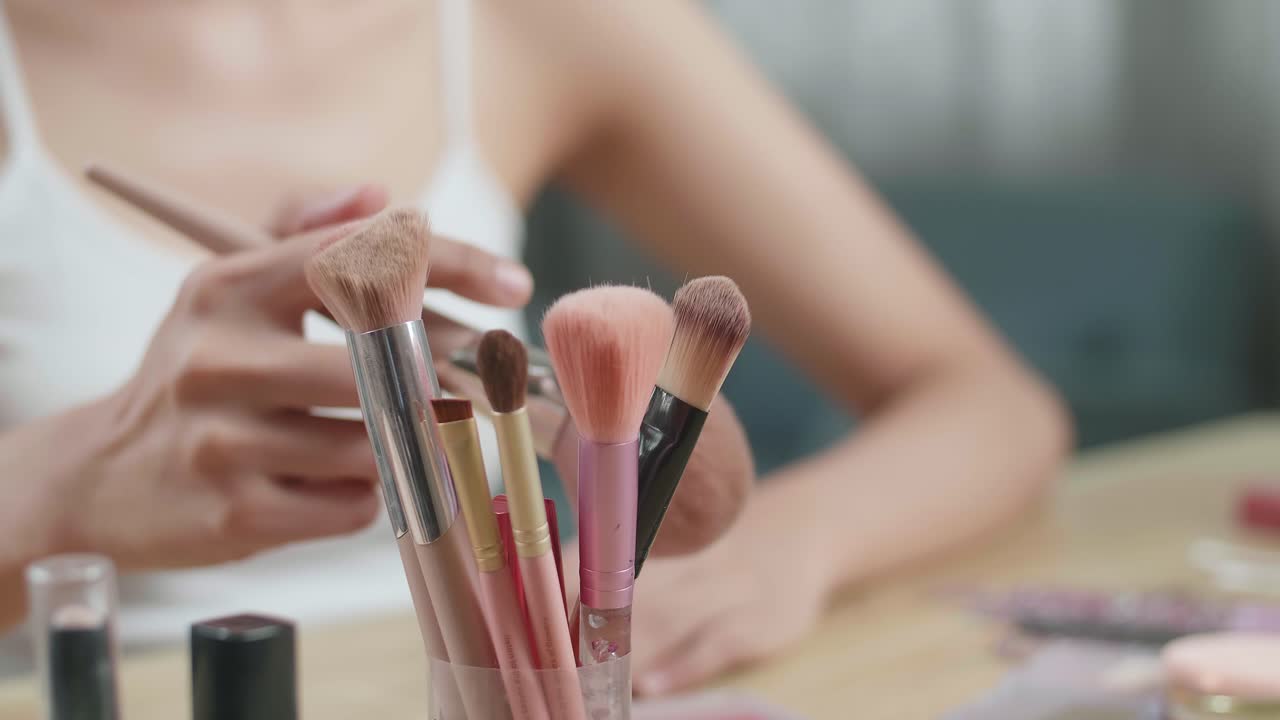 manos femeninas sosteniendo blusher en la vanidad y usándolo para aplicar maquillaje en casa