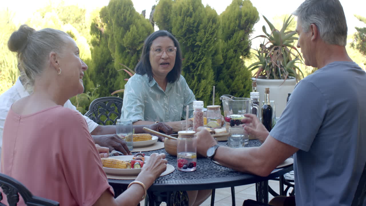 Senior diverse friends enjoying in garden lunch, sharing stories and laughter around table