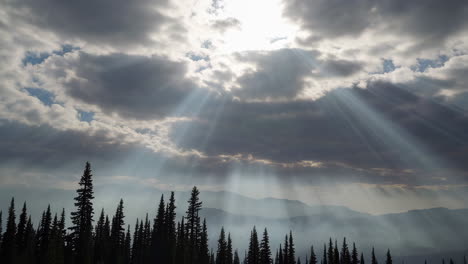 dramatic sunrays piercing through clouds over a silhouetted forest and misty mountains
