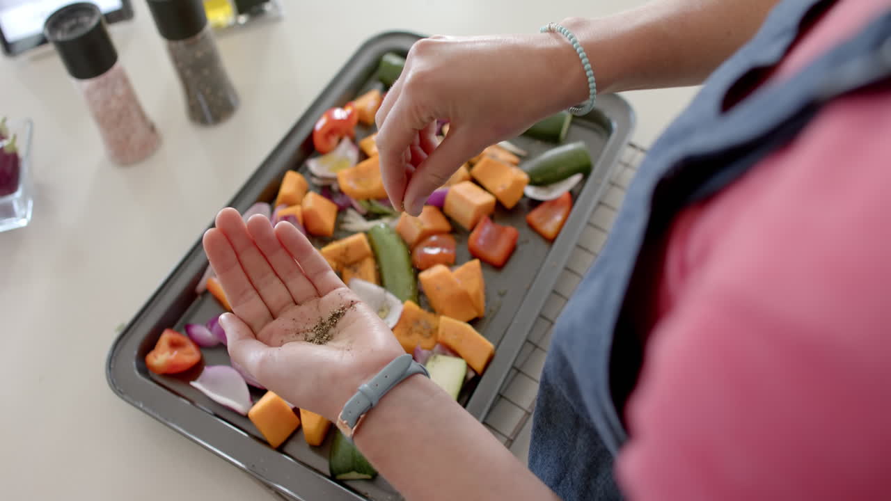 mujer diversa preparando verduras frescas y condimentos en la cocina, cámara lenta