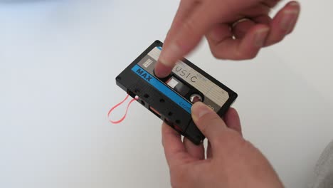 woman repairing retro audio cassette, winding tape by finger, white background, static