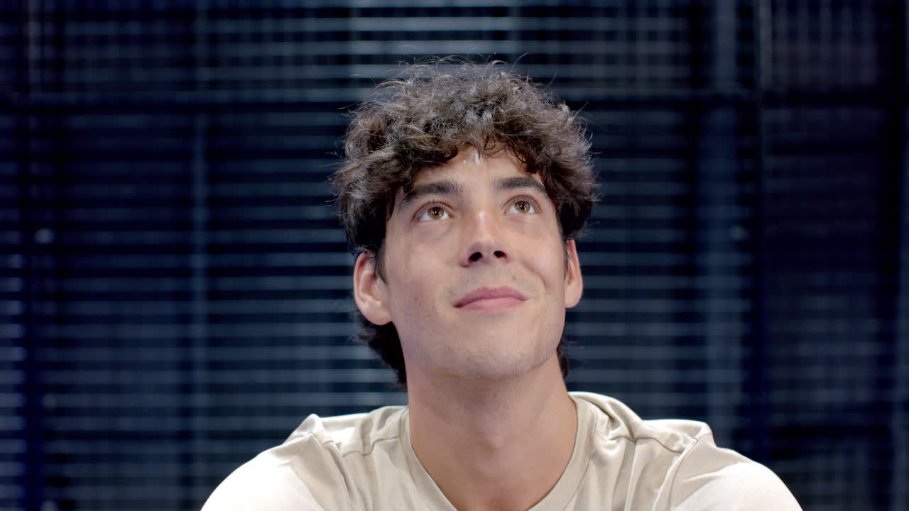 Young man with curly hair looking thoughtful, wearing casual shirt on indoor court, copy space