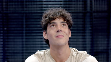 young man with curly hair looking thoughtful, wearing casual shirt on indoor court, copy space