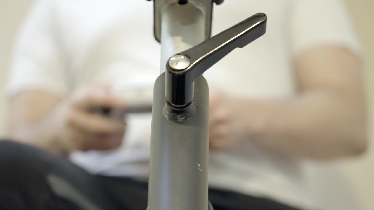 Person blurred in background using stationary bike, focus on lever