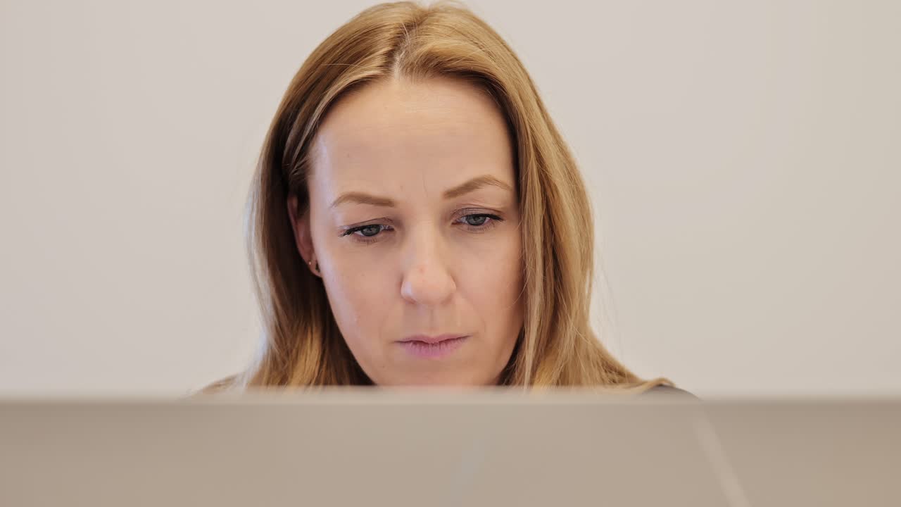 Close up portrait of thoughtful woman working on laptop indoors, serious focus