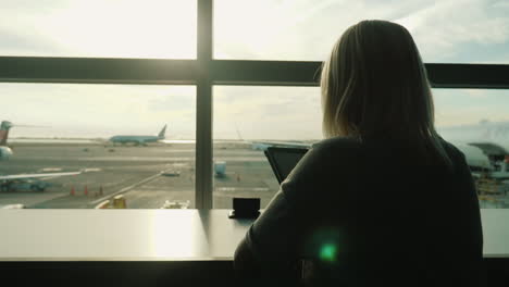 Mujer-Usando-Tableta-Por-La-Ventana-De-La-Terminal-Del-Aeropuerto