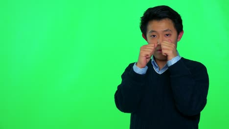 a young asian man looks at the  camera and shadow boxes - green screen studio