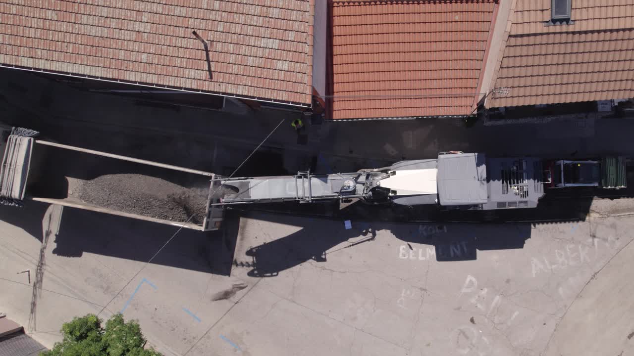 Aerial view looking down at heavy roadwork vehicle loading asphalt onto truck for road repair in Navas del Rey, Spain