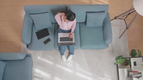 vista superior zoom out foto de una mujer estirándose mientras escribe en una computadora portátil en el sofá en casa