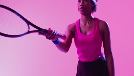 Video-of-focused-african-american-female-tennis-player-hitting-ball-on-neon-pink-lightning