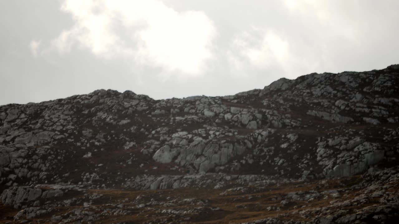 nubes blancas atmosféricas que pasan lentamente por encima del ominoso pico de la montaña rocosa