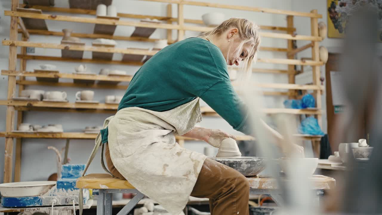 Female artist working at pottery workshop, sculpting crockery on pottery wheel, tracking shot, slow motion