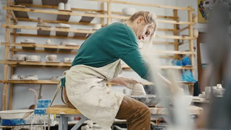 female artist working at pottery workshop, sculpting crockery on pottery wheel, tracking shot, slow motion