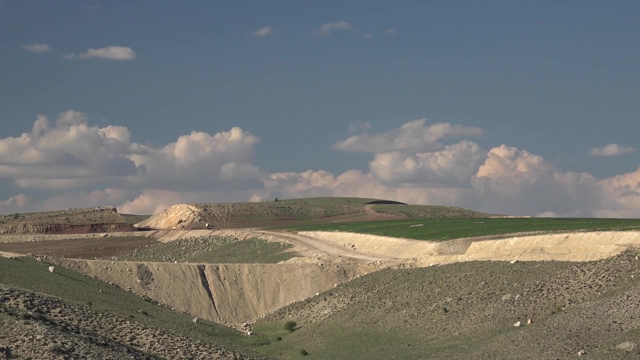 Colline ondulate e paesaggio aperto sotto un cielo azzurro nuvoloso