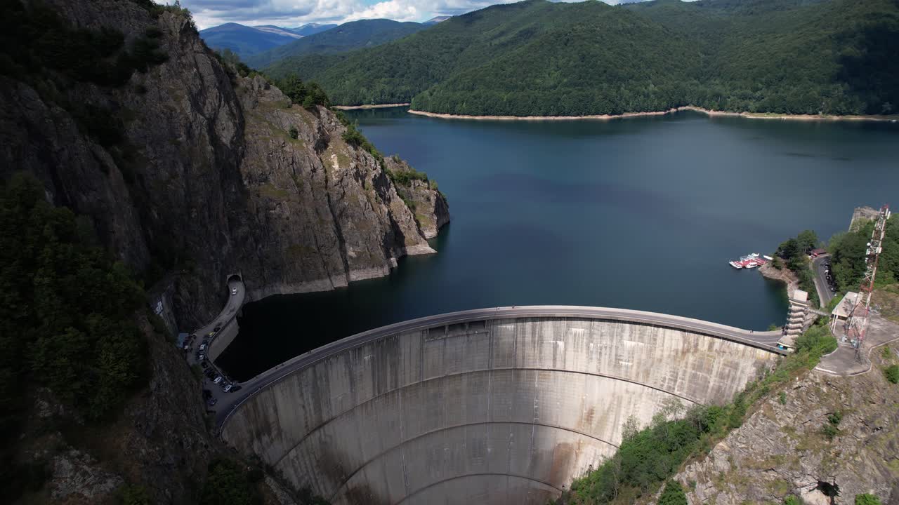 Aerial shot revealing Vidraru Dam and lake in Romania. Blue lake, dramatic curves, and green mountain backdrop in 4K.