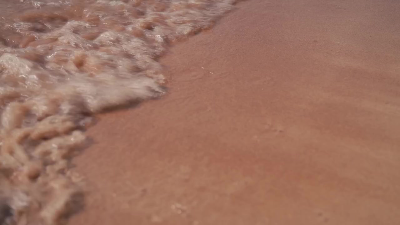 Nærbillede af små bølger, der slår ind mod sandstranden på Koh Tao-øen.