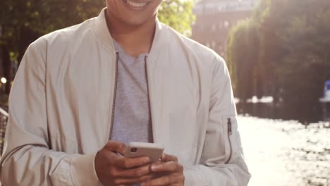 mid section young man texting and enjoying walk by canal