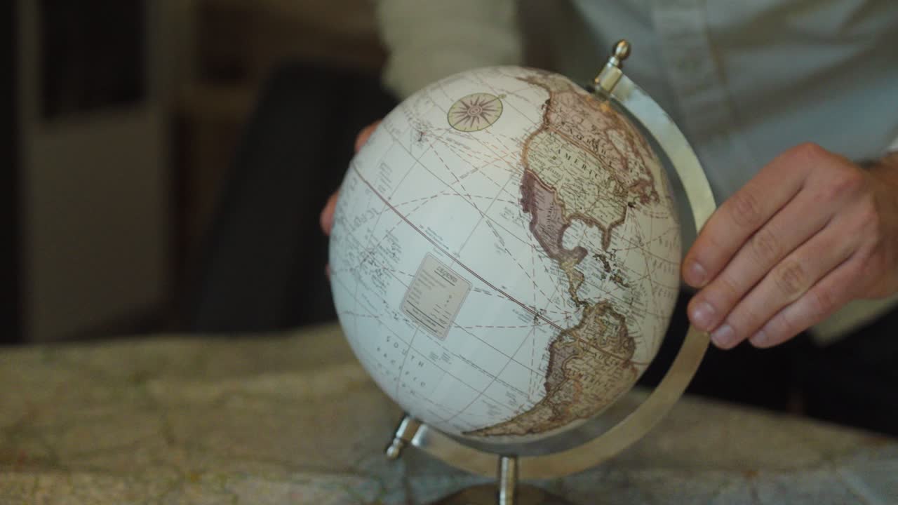 Close-up of hands gently spinning a vintage-style globe placed on a large map, symbolizing travel planning, world exploration, and global destinations
