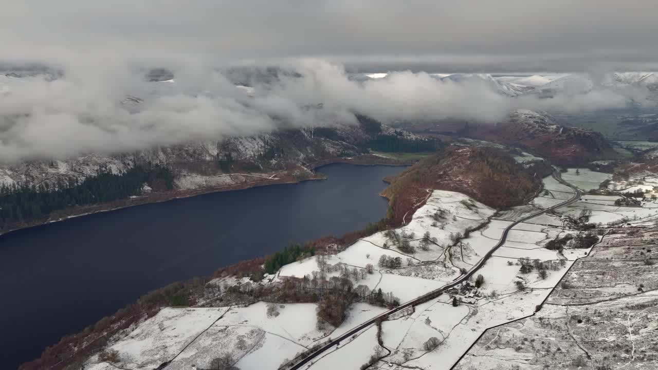 lago oscuro, paisaje ligeramente nevado, montañas cubiertas de nubes bajas, carretera con tráfico