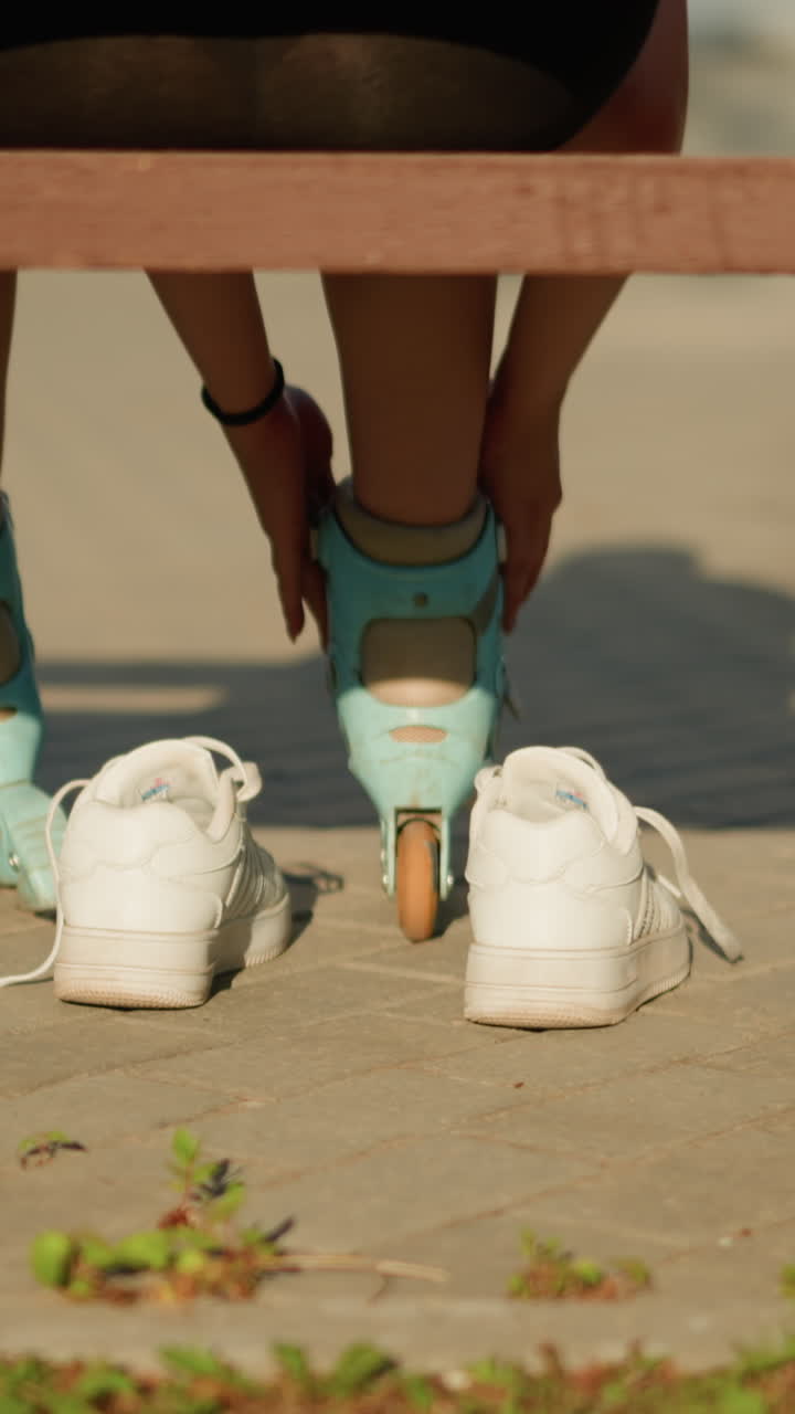 왼쪽 다리에 시안 롤러 스케이트에 을 조정하는 벤치에 앉아있는 개인의 뒷면, 따뜻한 빛이 보행자에 그림자를 던지는 동안,  스니커가 뒤에 휴식을 취하고, 초록색은 가장자리에서 어 봅니다.