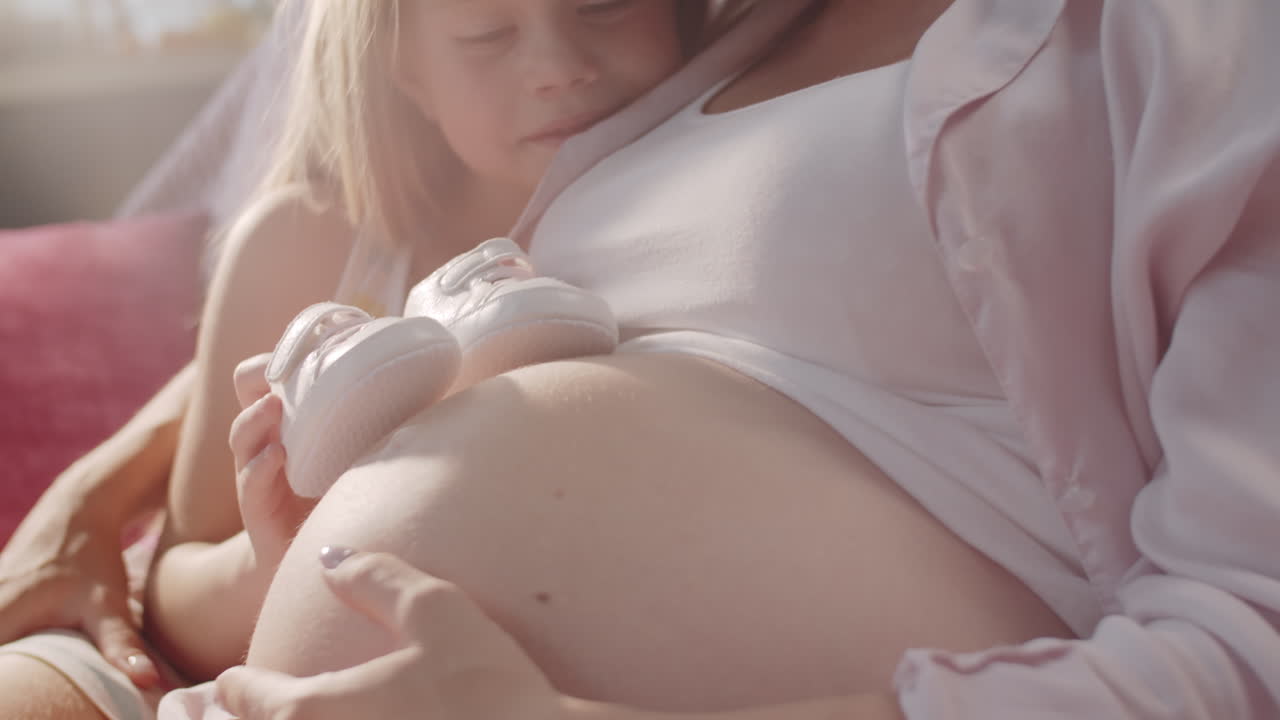 임신 한 어머니 와 딸 이 아기 의 신발 을 보고 있다