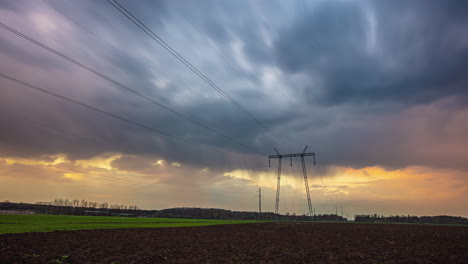 Golden-and-stormy-dark-clouds-mixing-above-power-lines-poles,-time-lapse