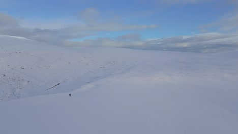 A man crossing a vast snow covered mountain alone.