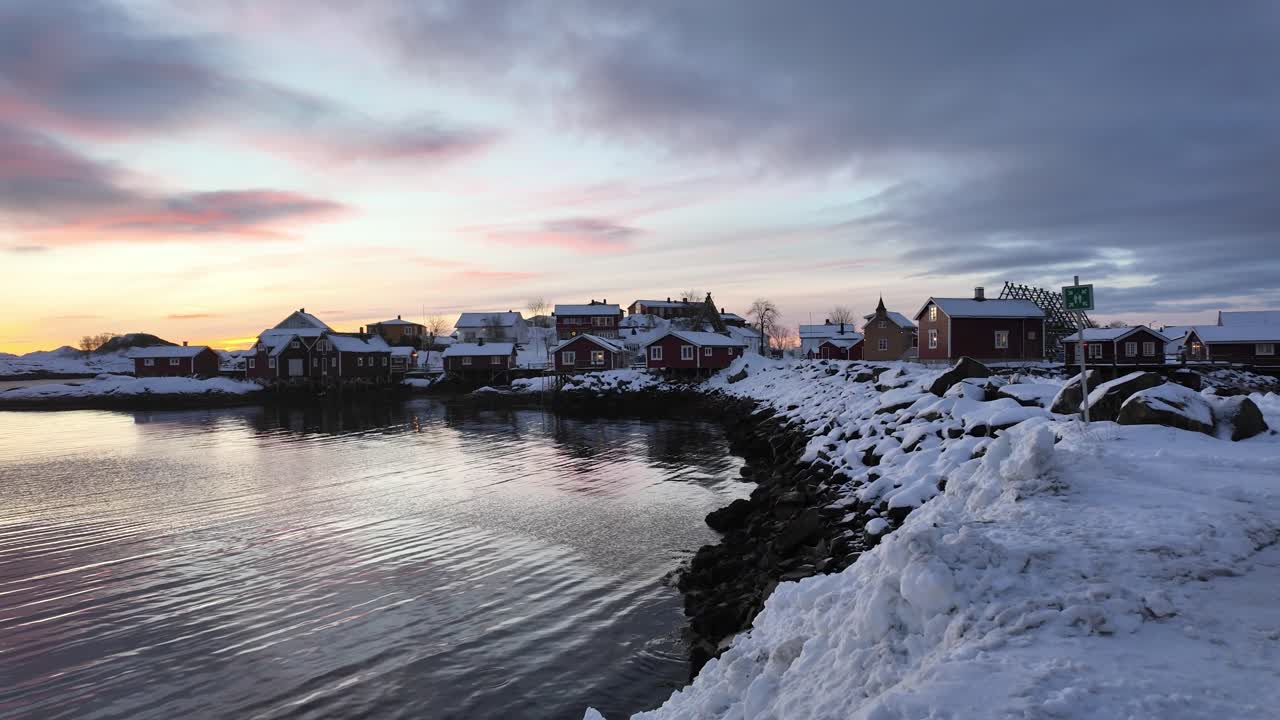 A serene coastal town in Svolvær during winter, with snowy houses at sunrise