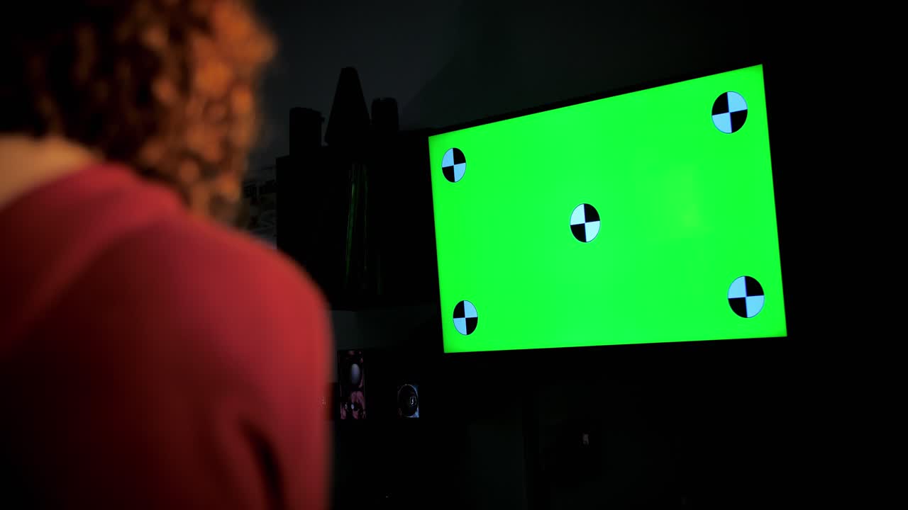 Persona che guarda un televisore con schermo verde in una stanza buia
