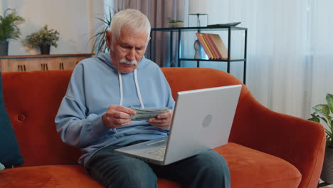 Smiling-happy-man-counting-money-cash-and-use-laptop-pc-calculate-domestic-income-earnings-at-home