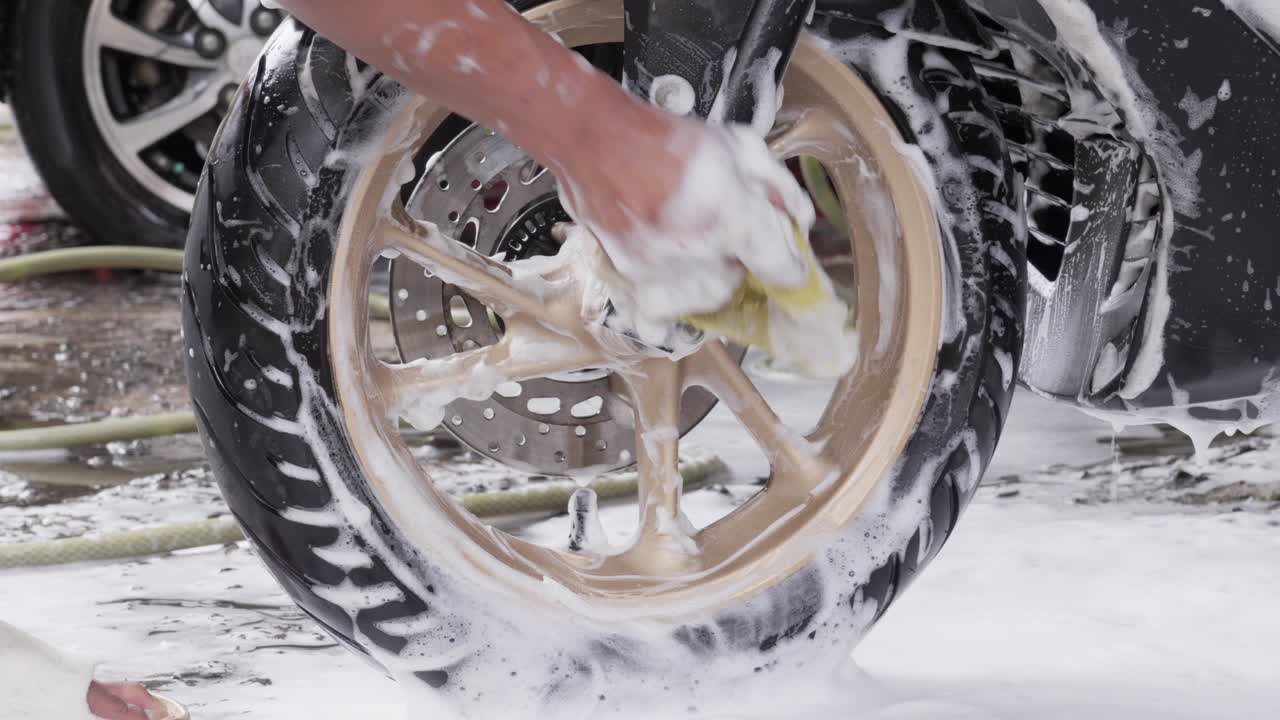 Hand cleaning a motorcycle wheel with foam during washing process, close-up shot