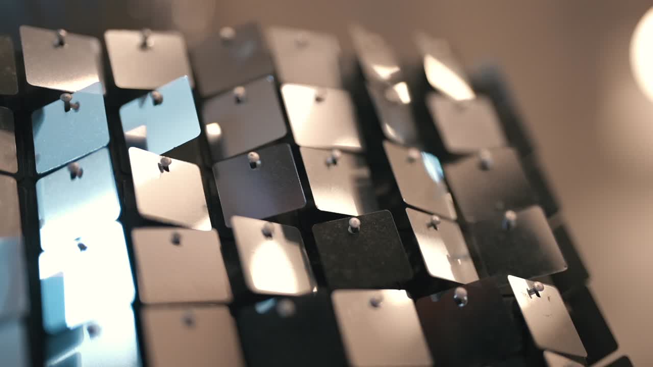 Un elegante dettaglio decorativo per feste mostra pannelli metallici riflettenti disposti secondo un motivo geometrico, catturando una luce ambientale soffusa per creare riflessi scintillanti, profondità e una raffinata atmosfera di lusso.