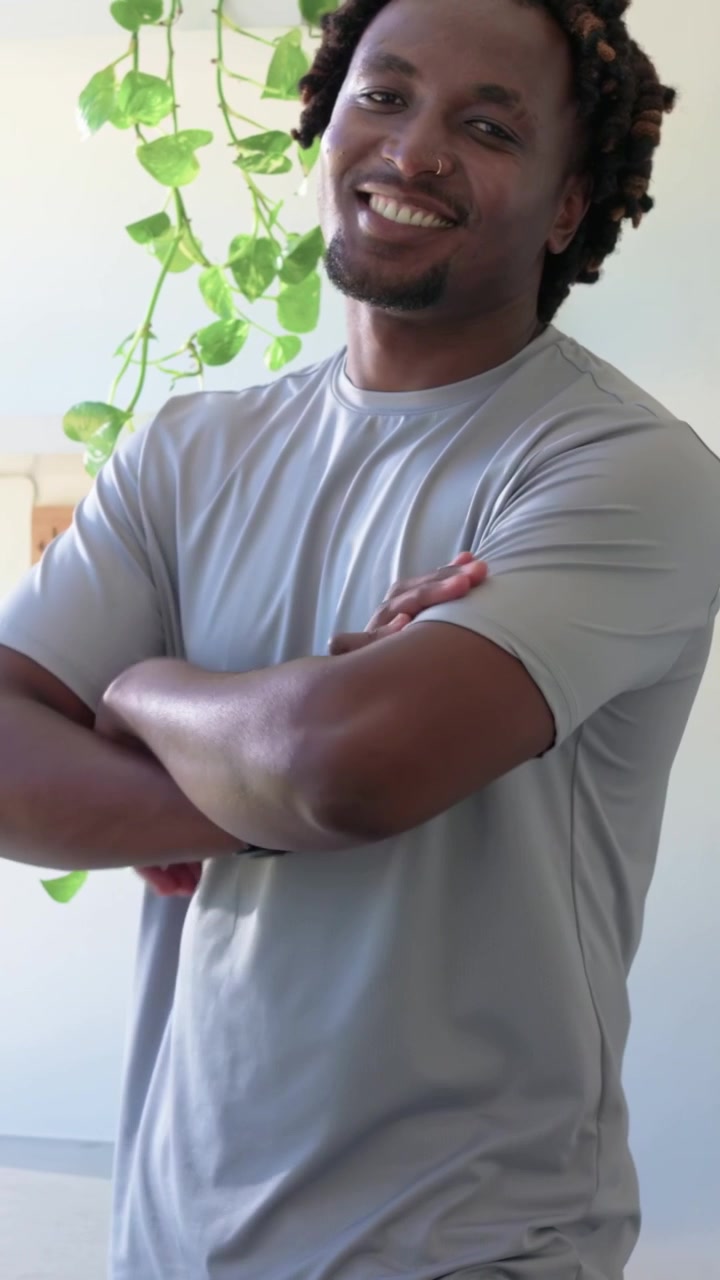 Vertical video: Turning man shifting leaning to smiling in kitchen, zooming showing gray tee, watch