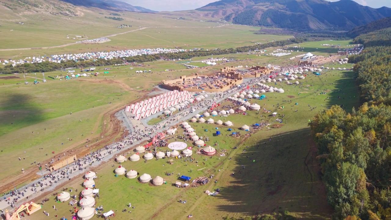 Ripresa con drone in avvicinamento sopra i turisti che osservano il vasto villaggio di yurte e l'area del festival ai World Nomad Games 2026 nella gola di Kyrchyn, Kirghizistan