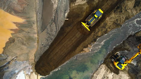 Aerial-top-down-shot-bulldozer-dragging-earth-parallel-to-a-water-channel-while-the-excavator-closes-the-channel