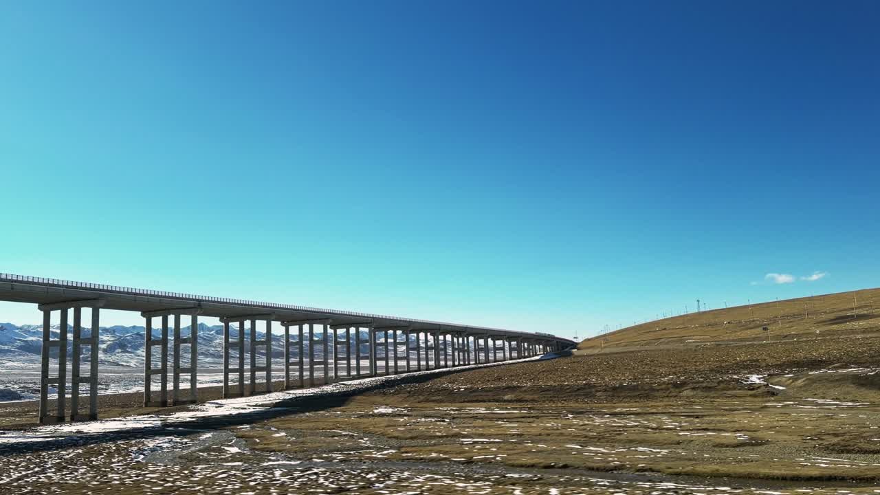 Along the Way, Qinghai and Gansu Province, China - A Long Elevated Bridge Stretches Across the Snowy Highland Plains Under a Clear Blue Sky - POV Shot