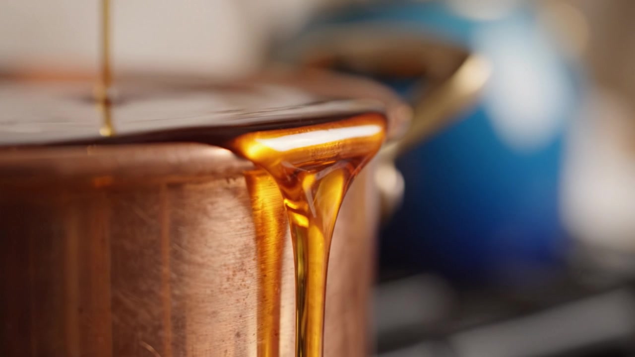 Miele luccicante che cola da un cucchiaio in una pentola di rame, mostrando la ricca tonalità ambrata e il fine dettaglio di una scena di cucina, delizioso e invitante.