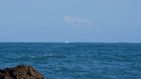 snow-covered mountain ranges in the south island of new zealand as seen from capital wellington in north island across the strait, with a small fishing boat in aotearoa