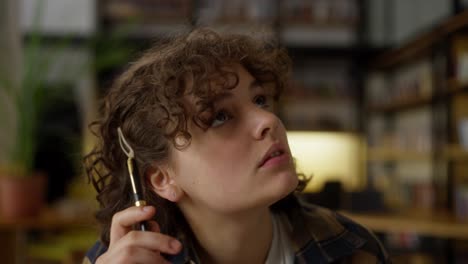 A-pensive-brunette-girl-with-curly-hair-looks-up-to-both-sides-while-thinking-at-the-table-in-the-library