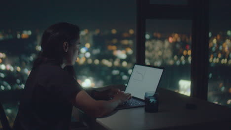 person working on a laptop at night with a city view