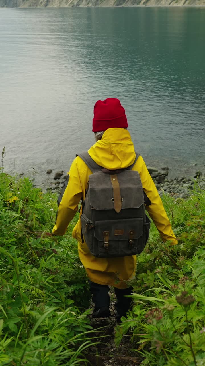 Escursionista con impermeabile giallo che scende verso la riva di un lago