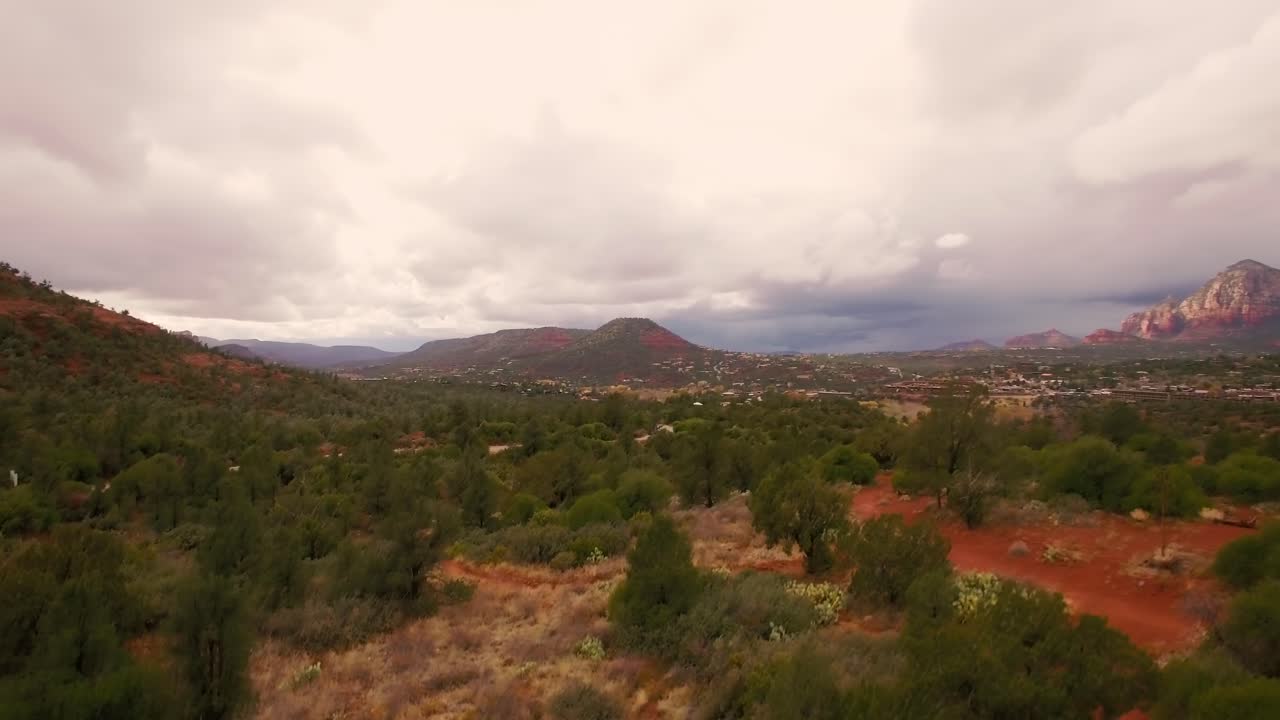 Aerial assent in the light rain from juniper tree forest in Coconino National Forest to a view of the grand red rock formations of Sedona, Arizona,