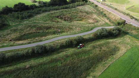 tractor in field driving near hedge and bush, aerial view above, far